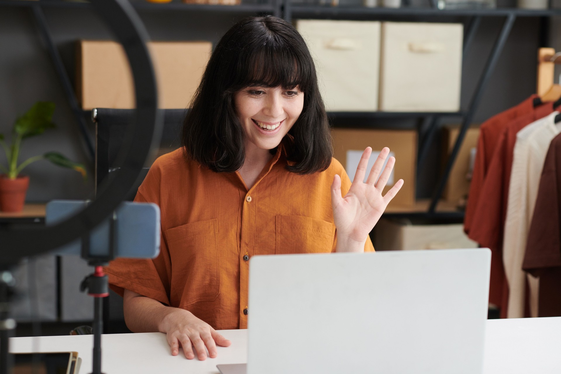 Happy young female blogger waving hand to online audience